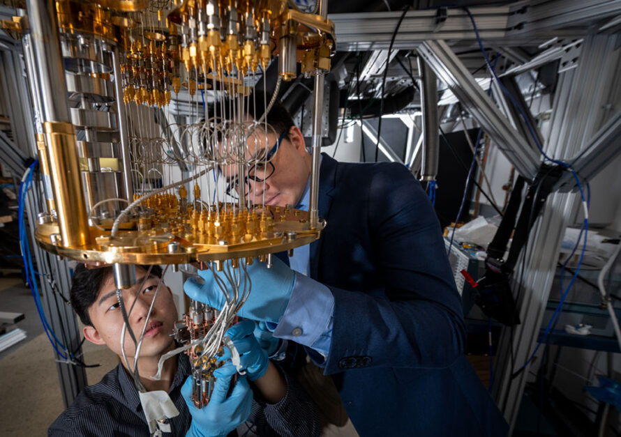 Two people examine a quantum computing system, adjusting gold and metal components with blue gloves in a laboratory.