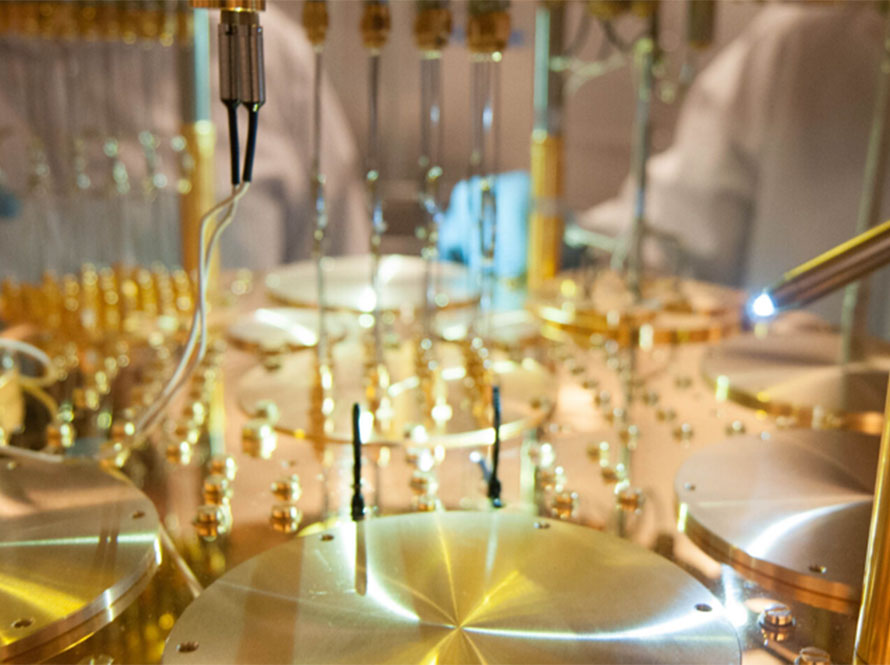 Close-up of intricate gold and metal components in a quantum computing system, with wires and probes extending from the equipment.